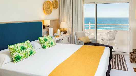 Hotellrum med dubbelsäng och havsutsikt från balkong. (AI-genererad text)