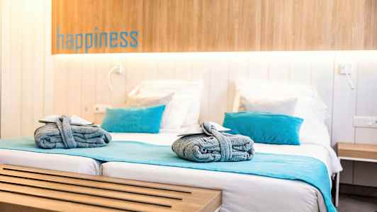 Ett hotellrum med en dubbelsäng, blåa detaljer som kuddar och överkast, samt hoprullade handdukar på sängen. (AI-genererad text)