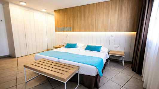 Ett hotellrum med en dubbelsäng, träpanel på väggen, turkosa textilier och bord vid sidan. (AI-genererad text)