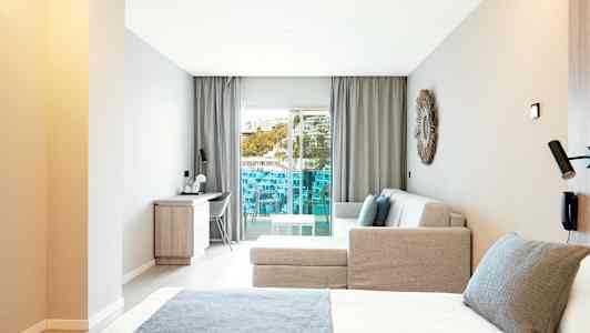 Modernt hotellrum med säng, soffa och skrivbord, samt en balkong med utsikt. (AI-genererad text)