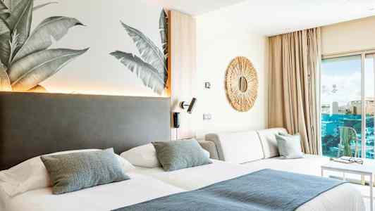 Hotellrum med två sängar, en soffa och en dekorativ spegel på väggen. (AI-genererad text)