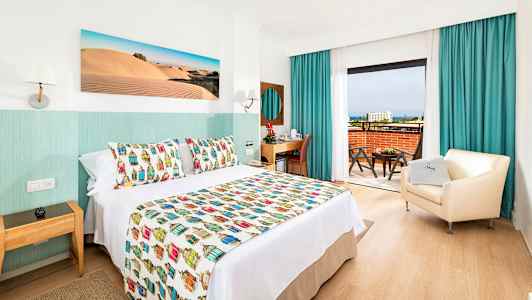 Hotelrum med dekorativt överkast, fåtölj och skrivbord samt utsikt från balkongen. (AI-genererad text)