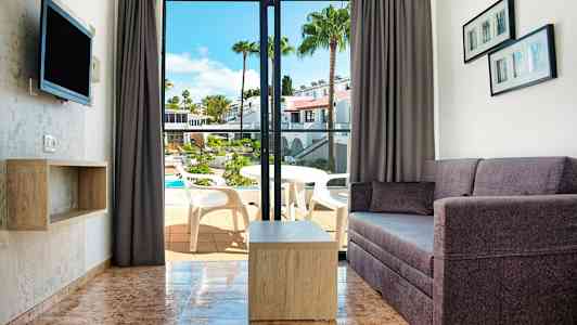 Vy av ett vardagsrum med soffa och bord samt en öppning till balkong med utsikt över en pool. (AI-genererad text)