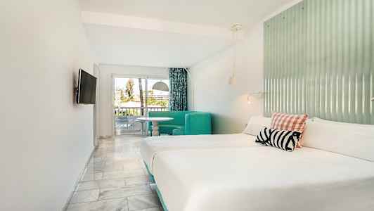 Hotellrum med dubbelsäng, sittgrupp och utgång till balkong. (AI-genererad text)