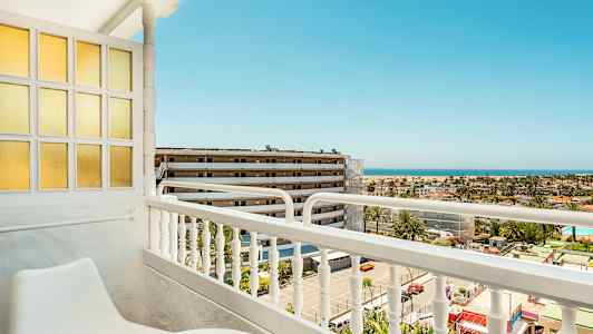 Utsikt från en balkong med sittmöbler, mot en byggnad och havet i bakgrunden. (AI-genererad text)