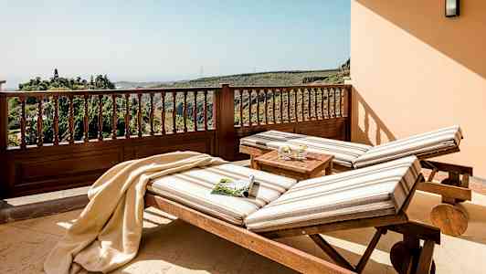 Två solstolar med randiga dynor står på en terrass med utsikt över grönskande kullar. (AI-genererad text)