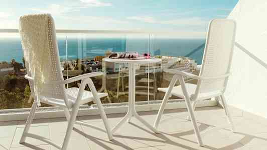Två vita stolar och ett bord på en balkong med utsikt över havet. (AI-genererad text)