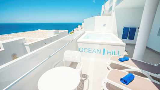 Terrass med utsikt över havet, solsängar, bord och en liten pool. (AI-genererad text)