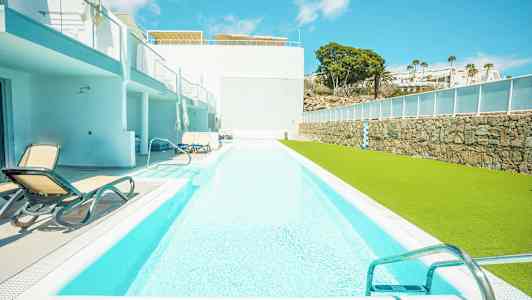 En lång swimmingpool med solstolar vid sidan och en grön gräsyta. (AI-genererad text)