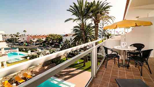 Utsikt från en balkong med sittmöbler och parasoll, med en pool och palmträd i bakgrunden. (AI-genererad text)