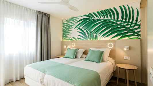 Dubbelrum med gröna sängkläder och bladmotiv på väggen. (AI-genererad text)