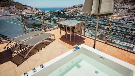 Terrass med solstolar, bord och utsikt över hav och stad. (AI-genererad text)