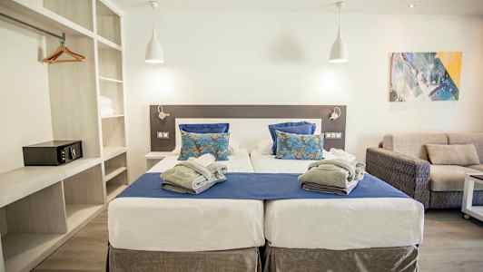 Dubbelrum med två enkelsängar, blåa och vita sängkläder samt grå filt. Modern inredning med soffa och välbelyst atmosfär. (AI-genererad text)