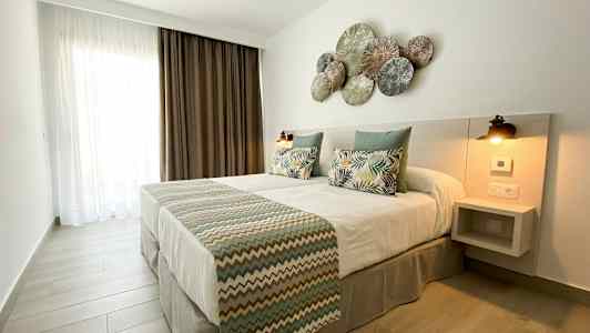 Ett sovrum med en dubbelsäng, prydnadskuddar och en dekorerad huvudgavel. (AI-genererad text)