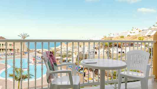 Utsikt från en balkong med vita möbler mot en pool och en havsutsikt. (AI-genererad text)