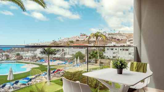 Utsikt från en balkong med utsikt över en pool och omgivande semesterutrustning under en solig dag. (AI-genererad text)