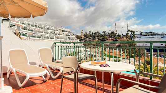 En terrass med två solstolar, ett bord och stolar samt utsikt över ett poolområde och palmer. (AI-genererad text)