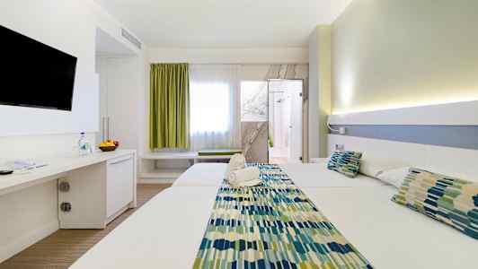 Ett hotellrum med två sängar, en TV på väggen, och en dörr till badrummet. Rummet har ljus inredning. (AI-genererad text)