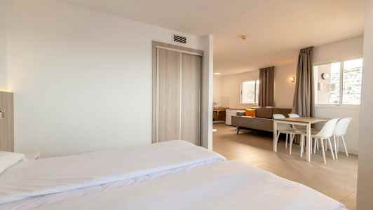 Modernt och ljust inrett hotellrum med dubbelsäng, sittgrupp och matbord. (AI-genererad text)