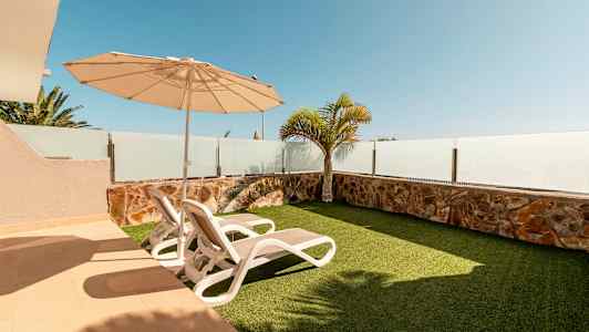 En uteplats med två solstolar, parasoll och konstgräs. (AI-genererad text)