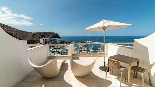 Terrass med utsikt över hamn och hav, utrustad med moderna stolar, bord och parasoll. (AI-genererad text)