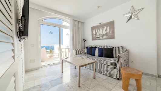 Svartvit inredning med soffa och bord i ett rum som har utsikt genom glasdörrar mot havet. (AI-genererad text)