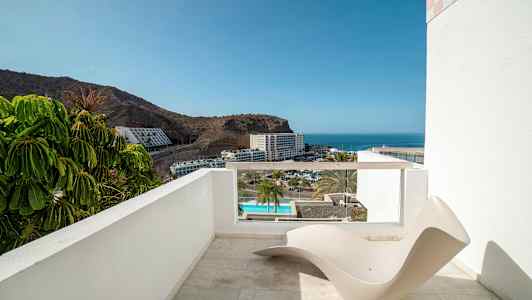 En terrass med utsikt mot havet och ett hotellområde, med en minimalistisk solstol i förgrunden. (AI-genererad text)