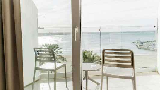 Utsikt från en balkong med två stolar och ett bord, mot en strand och havet. (AI-genererad text)