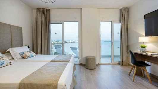 Hotellrum med två enkelsängar, skrivbord och havsutsikt genom glasdörrar. (AI-genererad text)