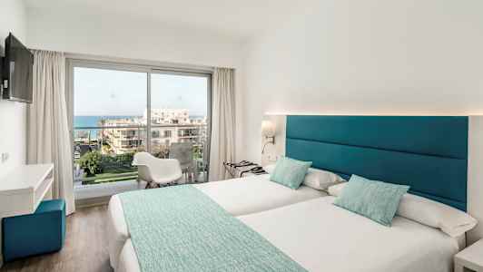 Ett ljust hotellrum med två enkelsängar, stora fönster och utsikt över havet. (AI-genererad text)