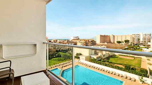 Balkong med utsikt över en swimmingpool och omgivande byggnader. Solstolar står vid poolen. (AI-genererad text)