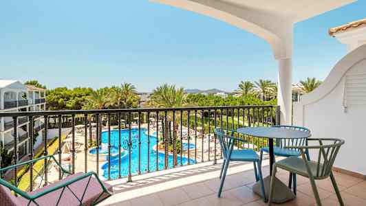 Utsikt från en balkong med bord och stolar mot en pool och omgivande grönska. (AI-genererad text)