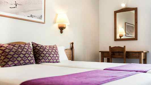 Ett hotellrum med två enkelsängar täckta med lila sängkläder, en spegel och ett skrivbord. (AI-genererad text)