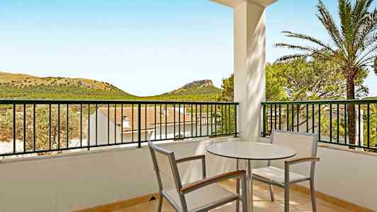 Balkong med bord och stolar, utsikt över landskap med kullar och grönska. (AI-genererad text)