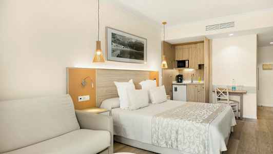 Ett hotellrum med en dubbelsäng, soffa och ett kök i bakgrunden. (AI-genererad text)