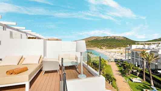 Utsikt över en terrass med solbäddar och stolar, med sandstrand och omgivande kullar i bakgrunden. (AI-genererad text)