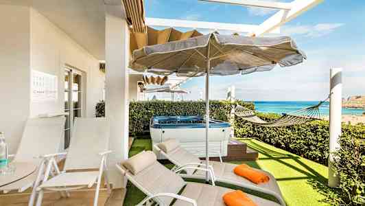 Terrass med solstolar, parasoll, jacuzzi och hängmatta samt utsikt över havet. (AI-genererad text)