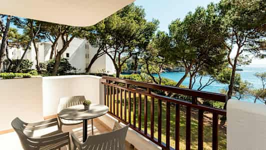 En balkong med bord och stolar, utsikt över träd och hav. (AI-genererad text)