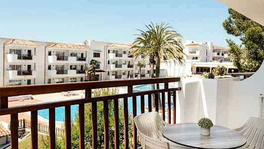 Utsikt från balkong med bord och stolar mot vit byggnad och poolområde. (AI-genererad text)