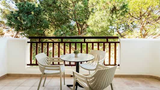 En balkong med fyra stolar och ett bord framför ett staket och gröna träd. (AI-genererad text)