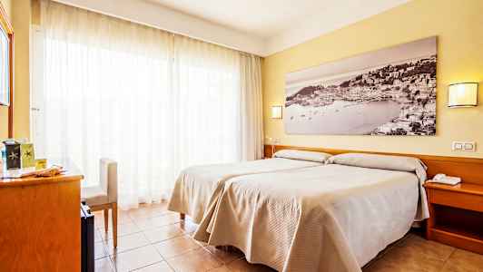 Ett hotellrum med två enkelsängar och en stor tavla på väggen. Rummet har ljusa gardiner och träinredning. (AI-genererad text)