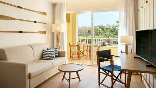 Ett rum med soffa, bord, och stolar. En dörr leder till en balkong med utsikt. (AI-genererad text)