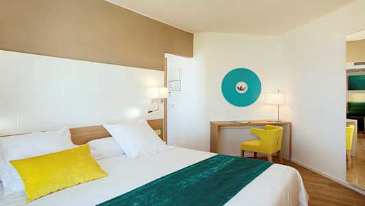 Ett modernt hotellrum med en säng i förgrunden, en skrivbordshörna med en gul stol och en blå dekorativ väggdetalj. (AI-genererad text)