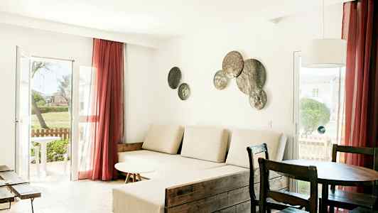 Ett vardagsrum med ljusa möbler, ett stort fönster med röda gardiner och dekorationer på väggen. (AI-genererad text)