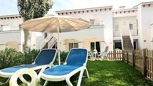 Två solstolar med en parasoll på en gräsmatta framför en vit byggnad. (AI-genererad text)