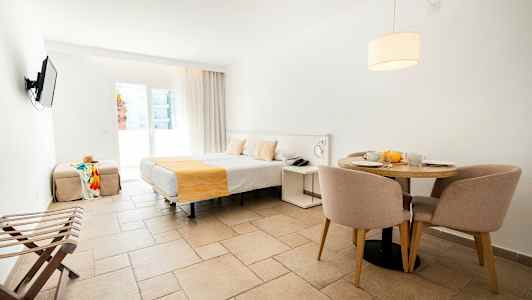 Ett hotellrum med en säng, ett matbord med stolar och en tv på väggen. (AI-genererad text)