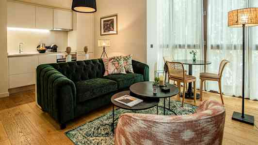 Ett vardagsrum med en grön soffa, ett soffbord och en matplats. Köksdelen syns i bakgrunden. (AI-genererad text)