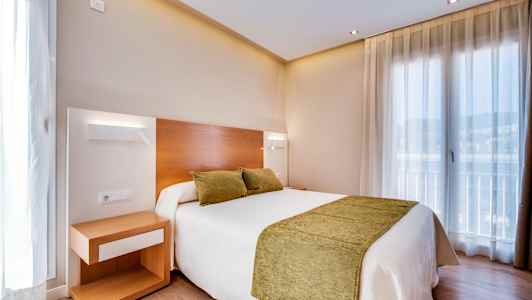 Ett hotellrum med en dubbelsäng med gröna kuddar och överkast. En nattduksbord står bredvid sängen. (AI-genererad text)