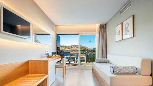 Ett modernt hotellrum med träinredning, soffa och utsikt över havet genom en glasdörr. (AI-genererad text)