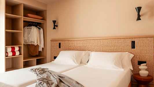 Ett hotellrum med två bäddar, vita sängkläder och en garderob till vänster. (AI-genererad text)